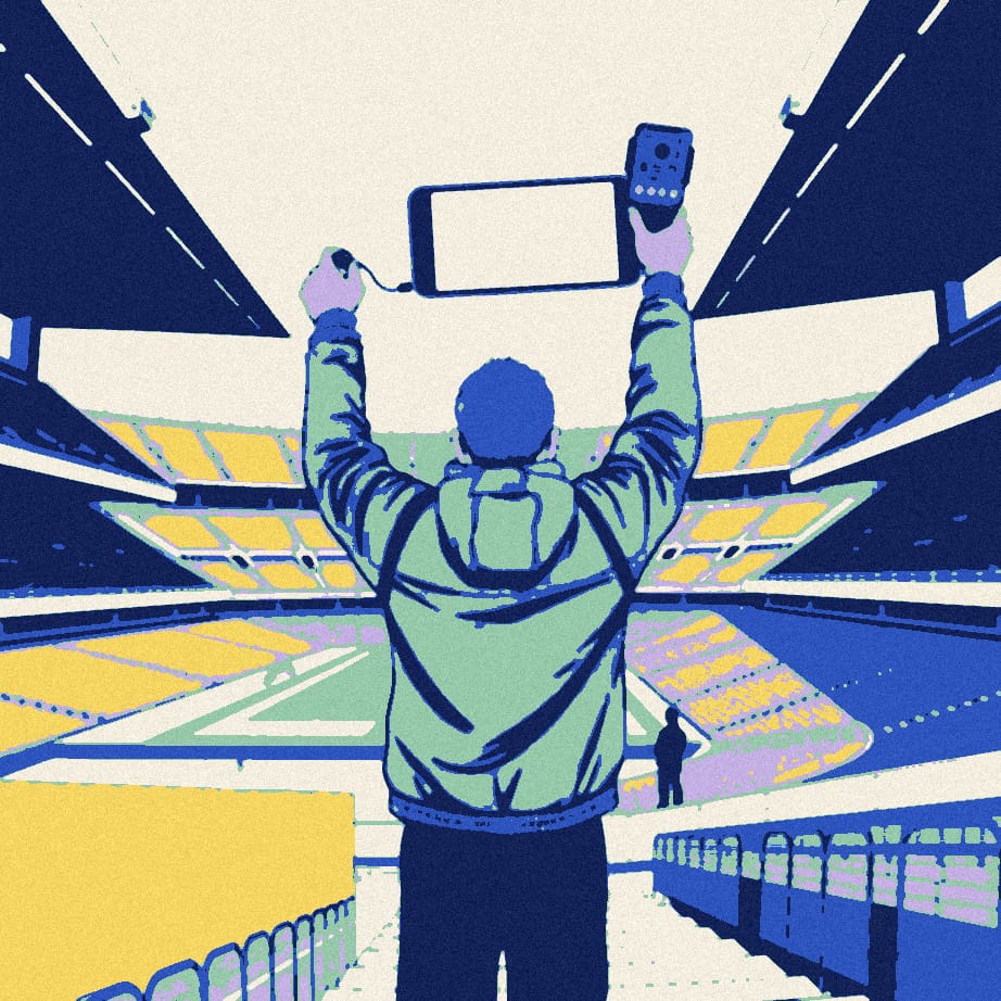 A tiny supporter outside a huge stadium films himself on an oversized camera rig while a faceless figure in a black padded jacket stands behind.