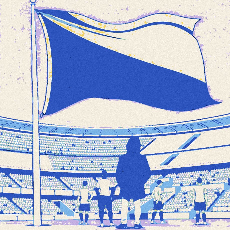 A tiny manager in a black jacket stands under a giant flag on a touchline while a few white-shirted players turn away.