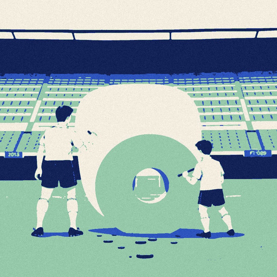 Two tiny footballers in white shirts chisel a huge stone slab into a neat round shape on a pitch while teammates look on.
