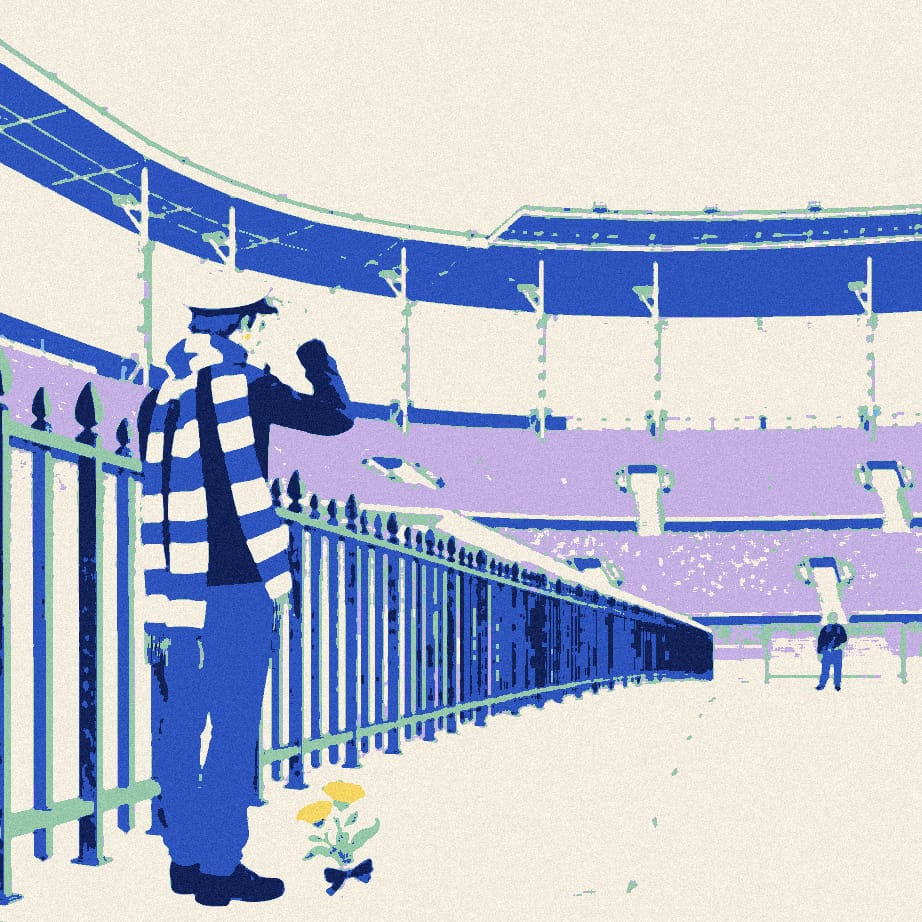 A fan seen from behind politely tips his cap to a row of iron stadium railings outside a sunlit ground.