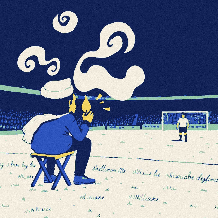 A tiny supporter seen from behind blows out a giant candle on a camp stool while a distant player stretches on a floodlit night pitch.