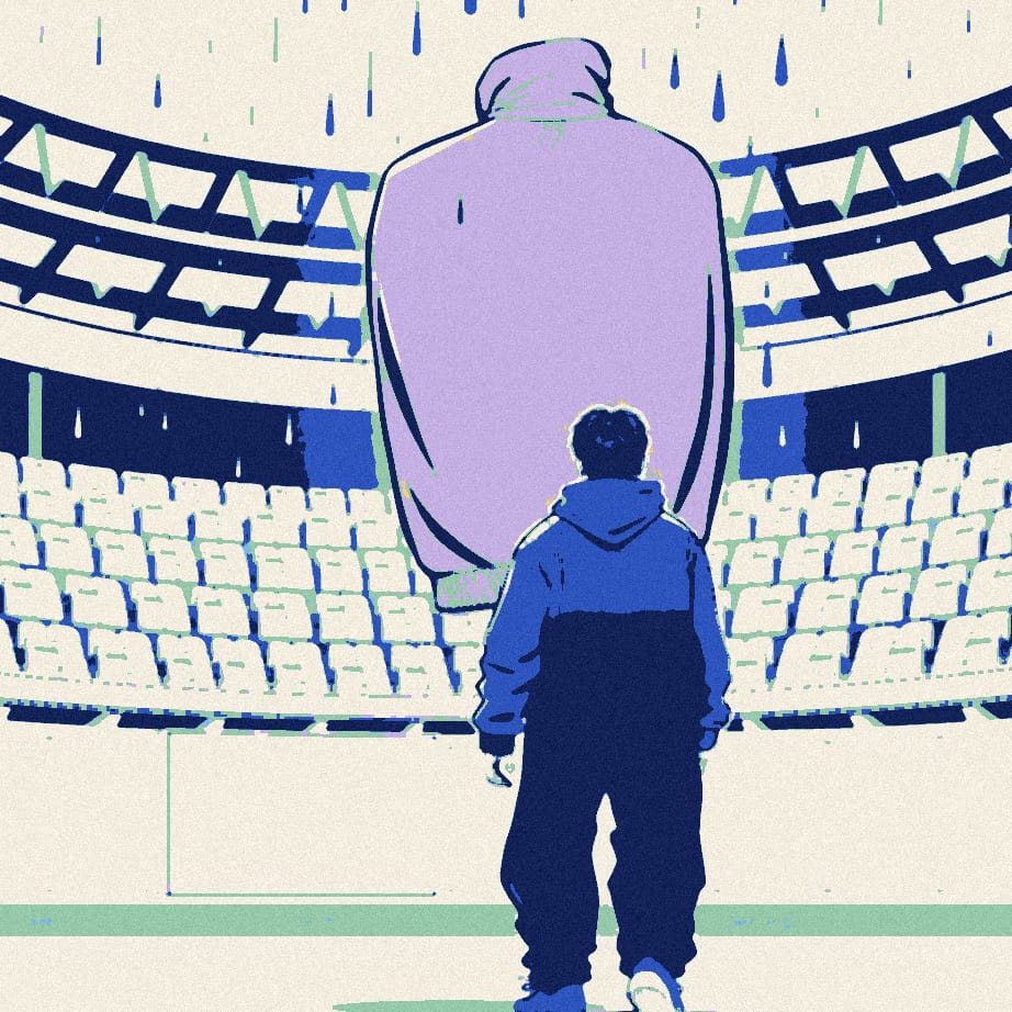 A tiny supporter seen from behind is swallowed by an enormous tracksuit top outside a vast stadium in the rain.