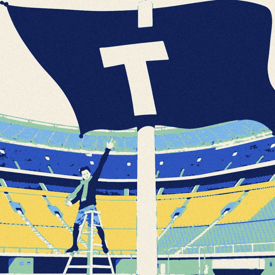 A tiny supporter on a stepladder holds a huge letter T up to a corner flag in an empty stadium.
